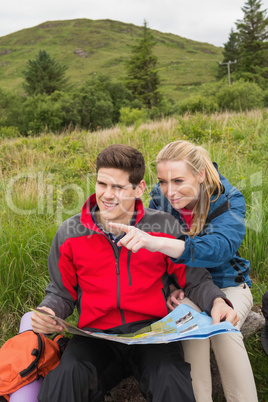 Cheerful couple taking a break on a hike to look at map with wom