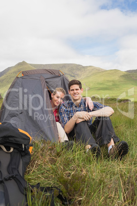 Happy couple sitting in their tent after a hike and looking at c