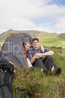 Happy couple sitting in their tent after a hike and looking at c