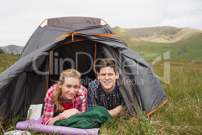 Happy couple lying in their tent after a hike and looking at cam