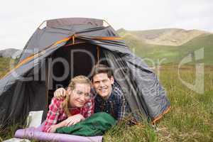Happy couple lying in their tent and looking at camera