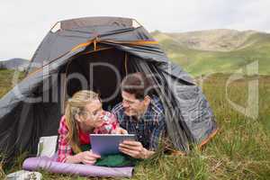 Happy couple lying in their tent and using digital tablet