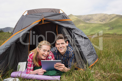 Smiling couple lying in their tent and using digital tablet