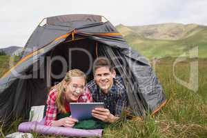 Smiling couple lying in their tent and using digital tablet