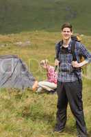 Happy man carrying backpack while girlfriend is pitching tent