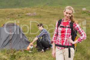 Cheerful woman carrying backpack while boyfriend is pitching ten