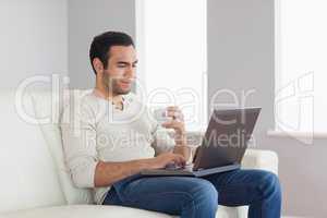 Relaxed attractive man holding coffee while working on his lapto