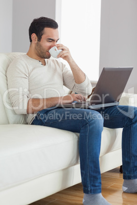 Relaxed attractive man drinking coffee while working on his lapt