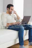 Relaxed attractive man drinking coffee while working on his lapt