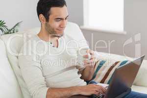 Calm attractive man drinking coffee while working on his laptop