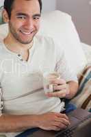 Smiling attractive man drinking coffee while using his laptop