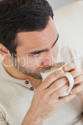 Thoughtful handsome man drinking coffee while relaxing on sofa