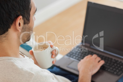 Handsome man drinking coffee while using his laptop