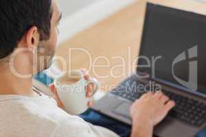 Handsome man drinking coffee while using his laptop