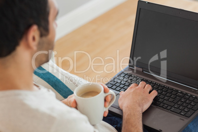 Brown haired man holding coffee using his laptop