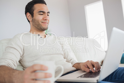 Peaceful handsome man having coffee while using his laptop