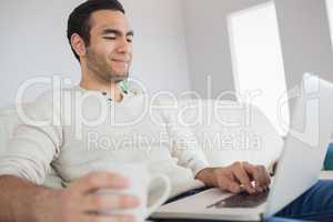 Peaceful handsome man having coffee while using his laptop