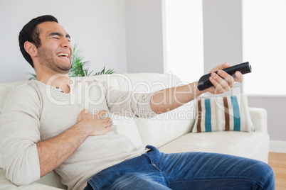 Handsome man bursting out laughing while watching tv