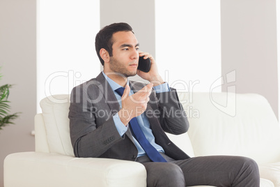 Serious businessman on the phone sitting on cosy sofa