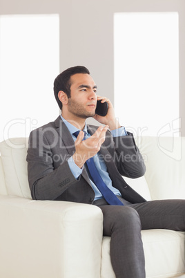 Serious businessman having a phone call sitting on cosy sofa