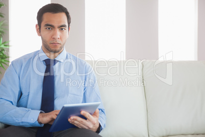 Unsmiling classy businessman using tablet pc