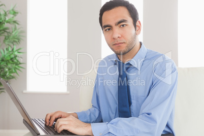 Serious classy businessman using his laptop while sitting on cos