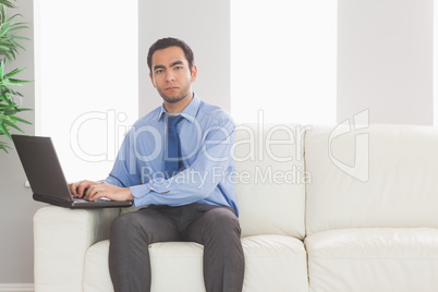 Stern businessman using his laptop while sitting on cosy sofa