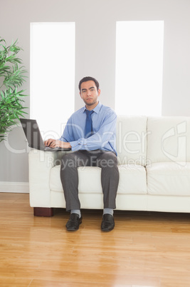 Stern young businessman using his laptop while sitting on cosy s