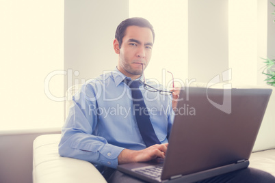 Nervous man biting his eyeglasses and using a laptop