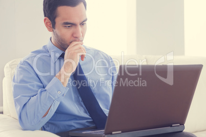 Stressed man using a laptop sitting on a sofa