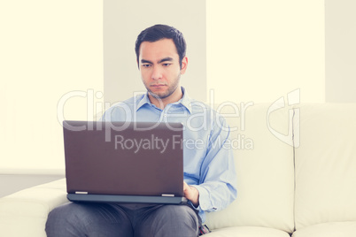 Bored man using a laptop sitting on a sofa