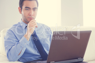 Annoyed man using a laptop sitting on a sofa