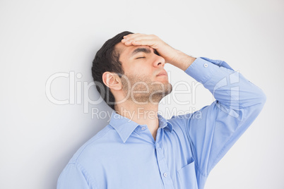 Irritated man with hand on forehead leaning against a wall