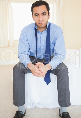 Unsmiling man sitting on his bed