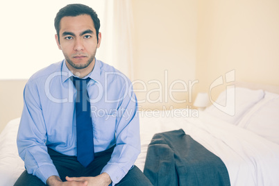 Frowning man looking at camera sitting on his bed