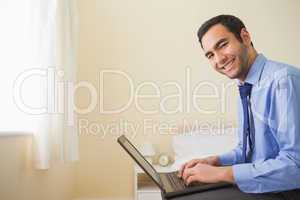 Smiling man using a laptop sitting on a bed