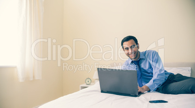 Content man lying on a bed using a laptop