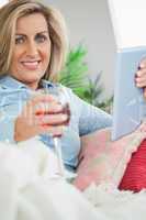 Smiling woman lying on a sofa drinking wine and using a tablet p