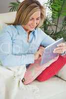 Smiling woman lying on a sofa using a tablet pc