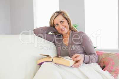 Smiling woman holding a book and lying on a sofa