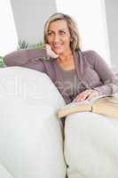 Smiling woman holding a book and lying on a sofa