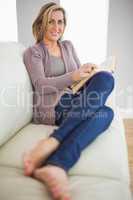Smiling woman holding a book lying on a sofa