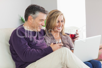 Happy couple watching their laptop and drinking wine