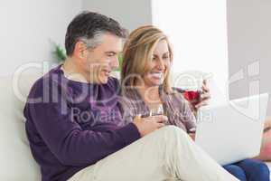 Happy couple watching their laptop and drinking wine
