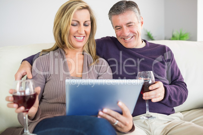 Happy couple watching their tablet pc and drinking wine