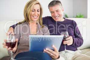 Happy couple watching their tablet pc and drinking wine