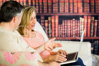 Happy couple sitting on a sofa in a reading room watching a lapt