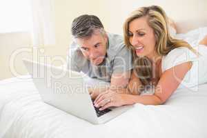 Happy couple lying on a bed watching a laptop