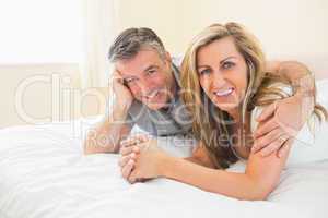 Happy couple lying on a bed looking at camera