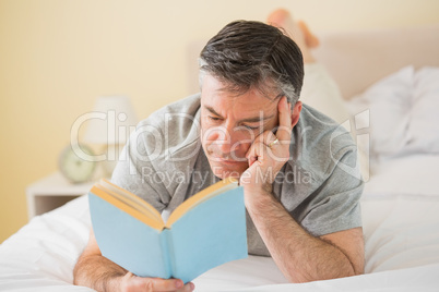Concentrated man reading a book on his bed